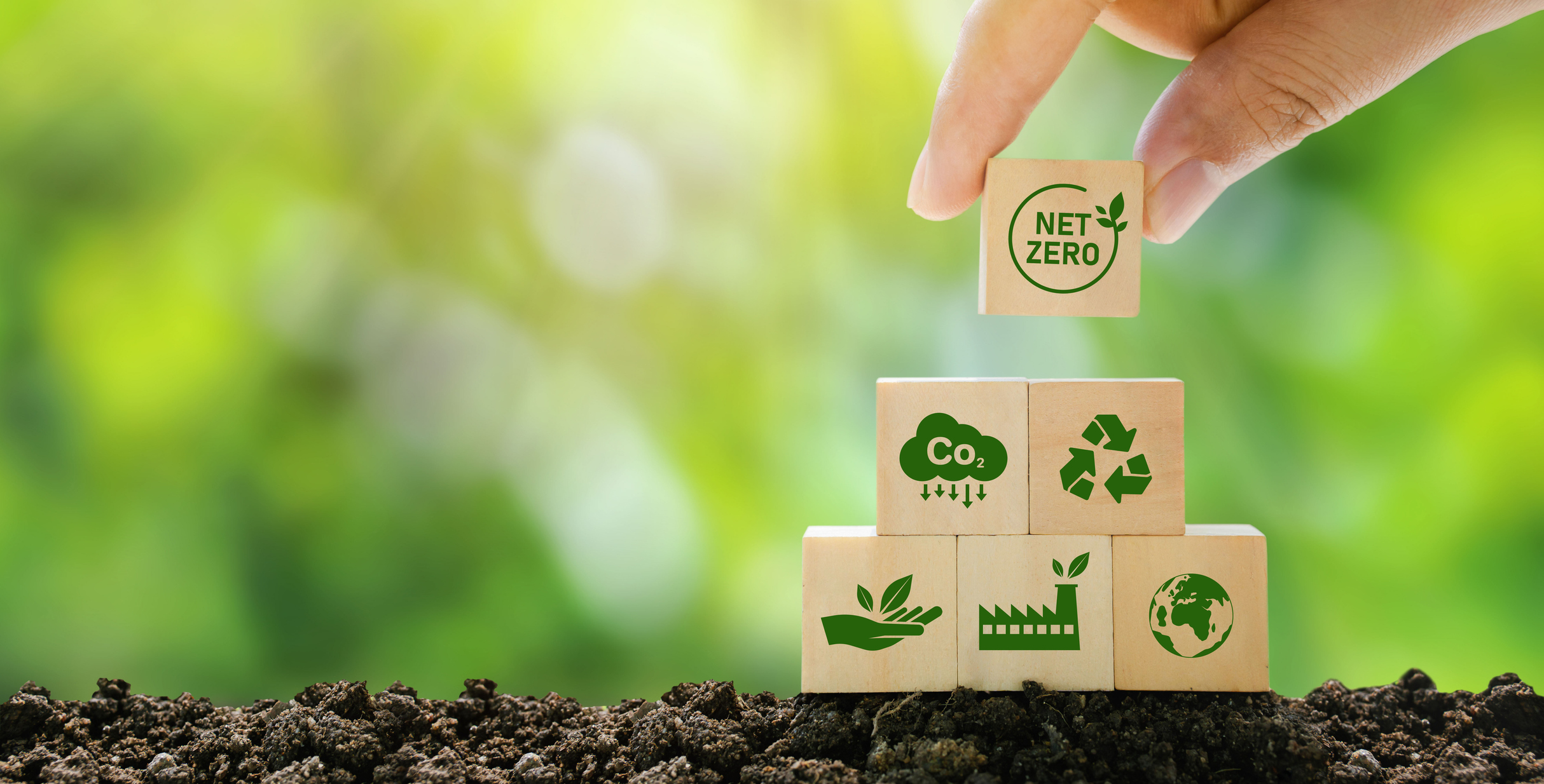 Hand stacking wooden blocks with green icons for net zero, recycling, CO₂ reduction, and sustainability.