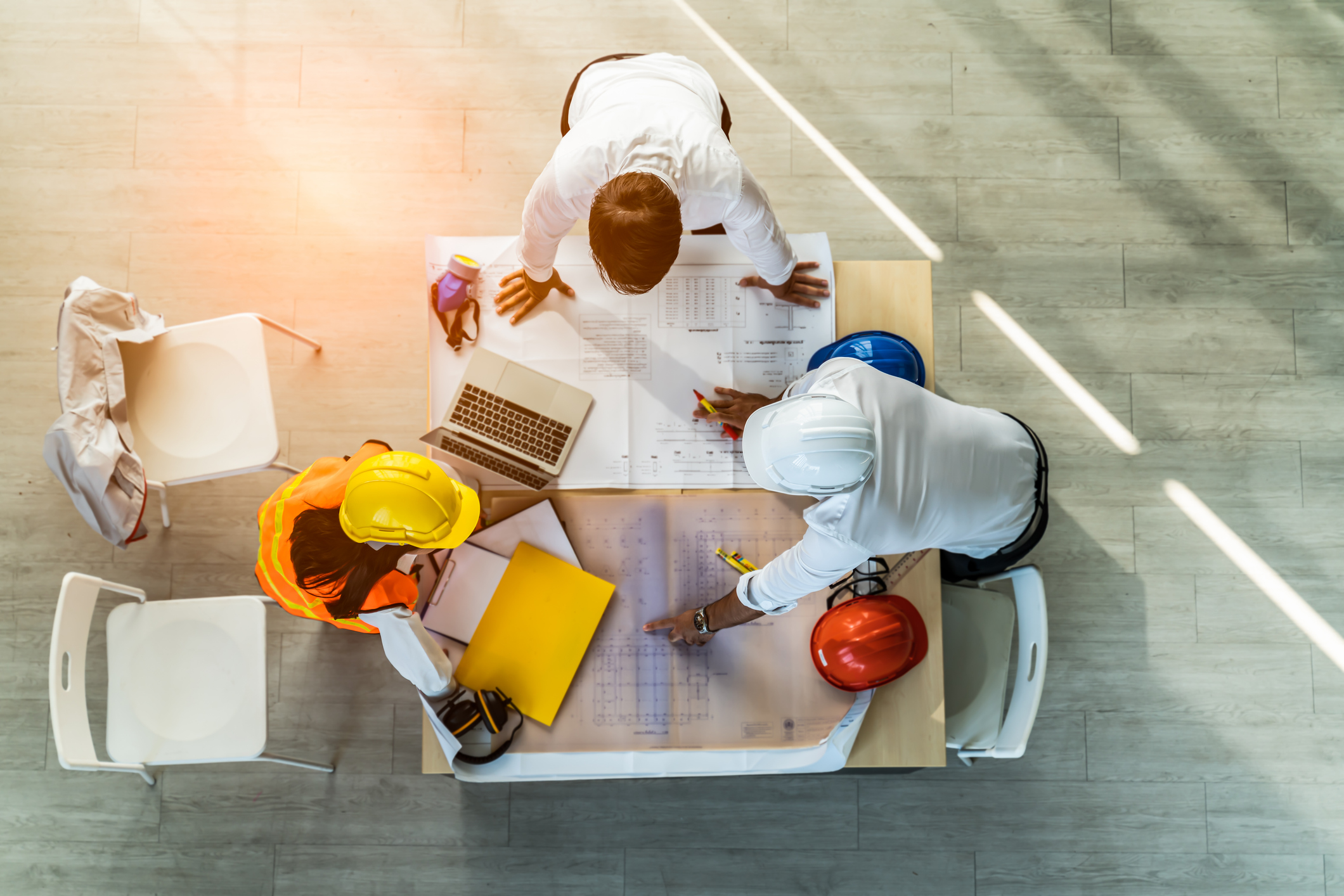 Top-down view of engineers and workers in hard hats collaborating over blueprints and documents on a desk.