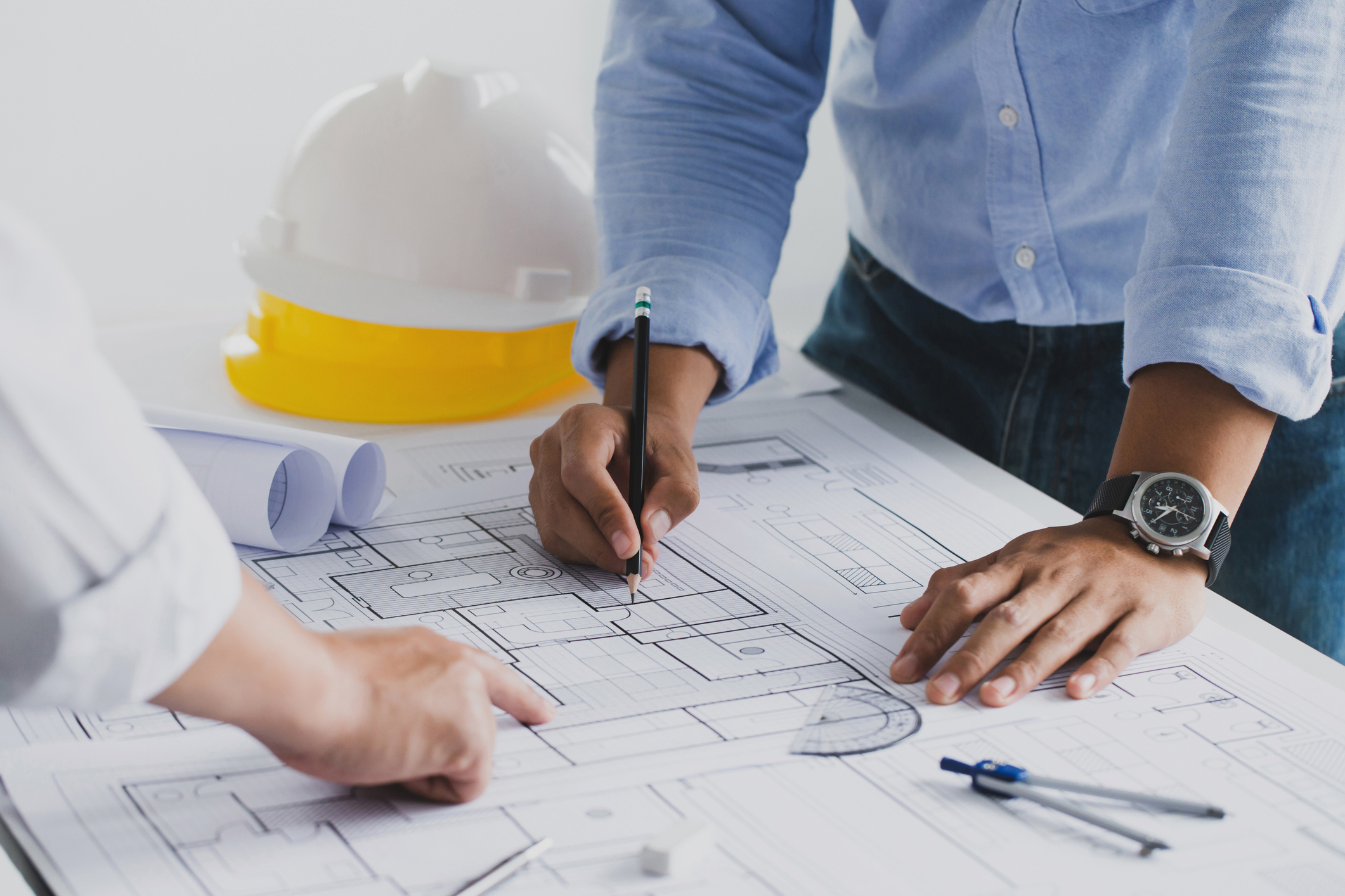 Close-up of engineers reviewing architectural blueprints with safety helmets and drafting tools on the table.