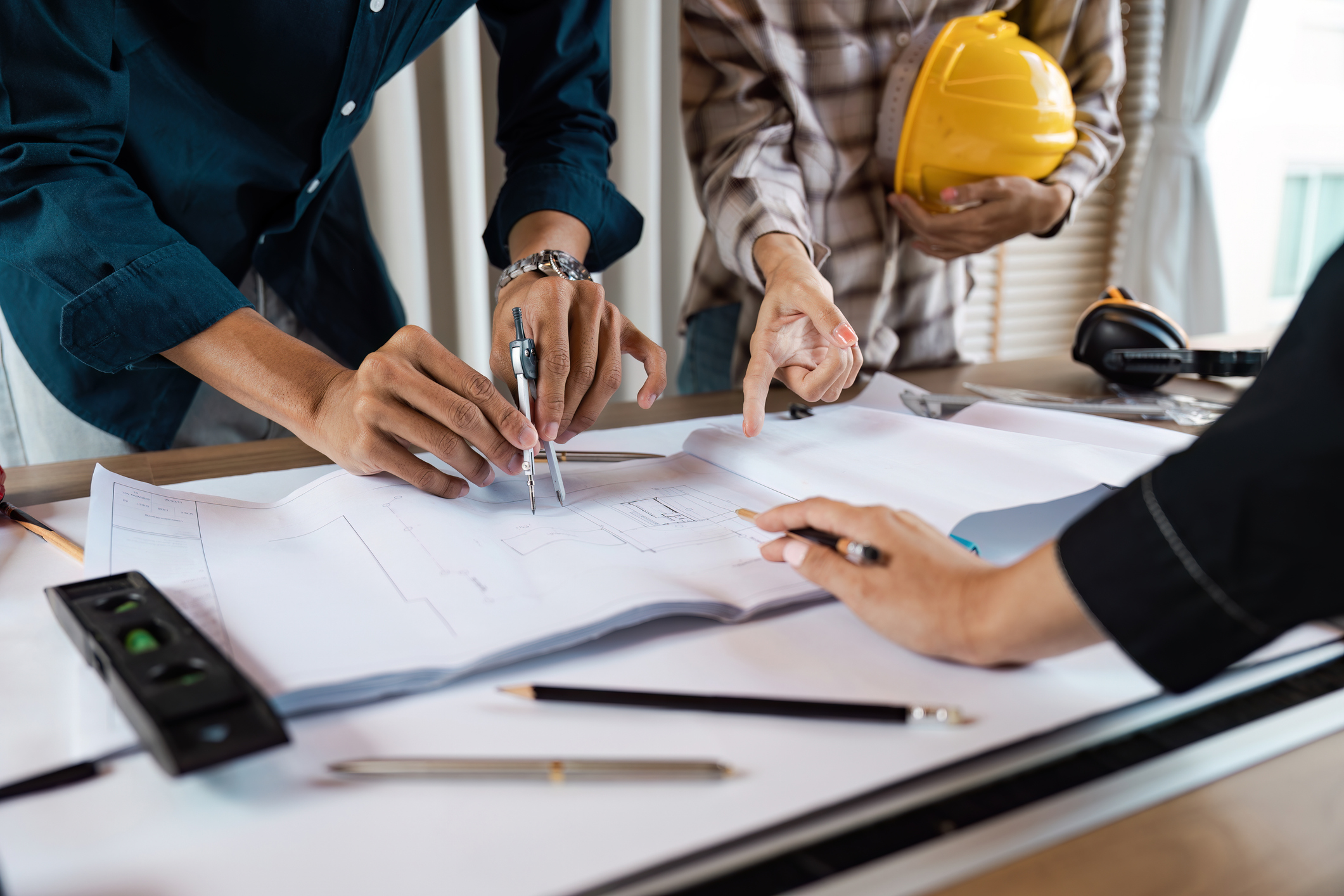 Construction team discussing building plans with compasses and pointing at detailed architectural drawings.