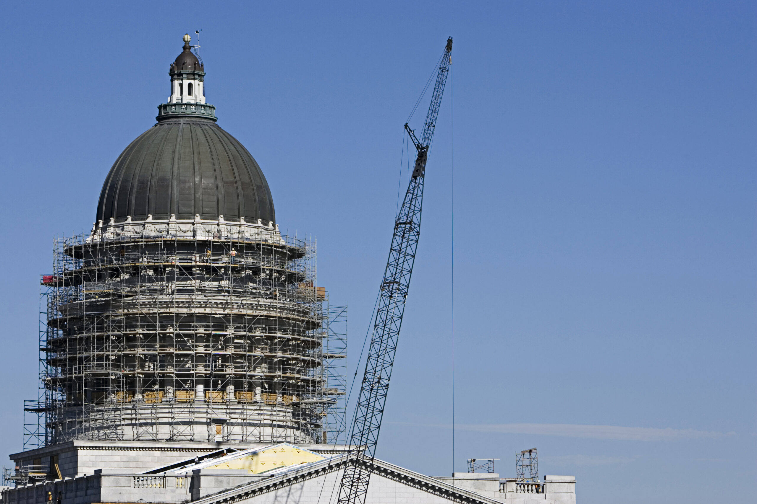 Historic domed building surrounded by scaffolding during restoration work, with a large construction crane beside it.