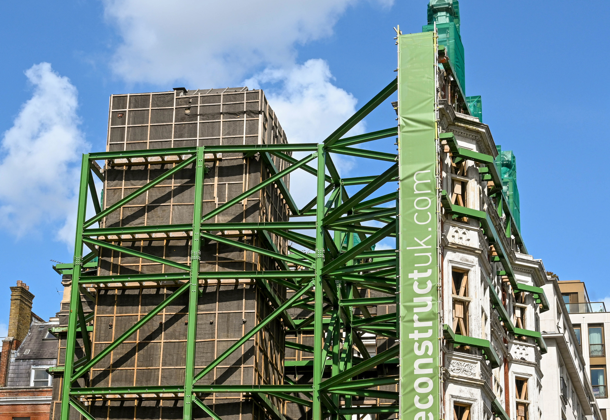 Partially deconstructed historic building supported by green external steel framework during renovation works.