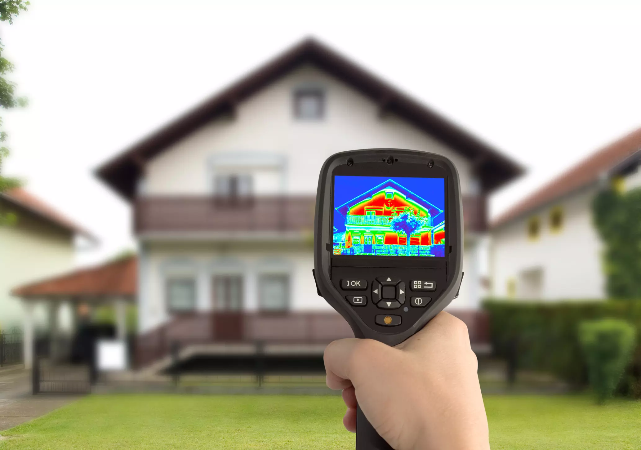 Person holding a thermal imaging camera aimed at a house, with heat loss areas displayed in red and yellow.