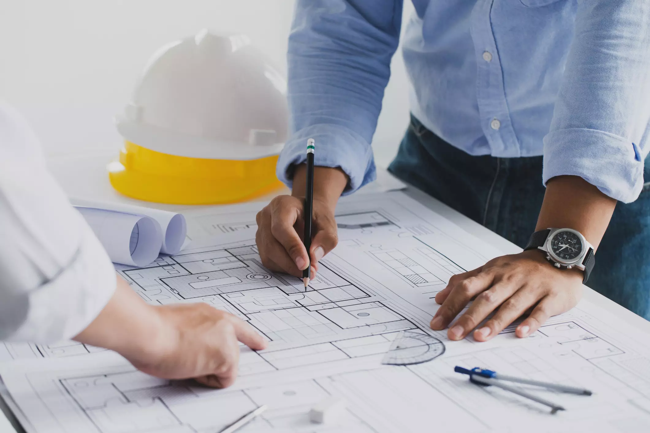 Close-up of engineers reviewing architectural blueprints with safety helmets and drafting tools on the table.