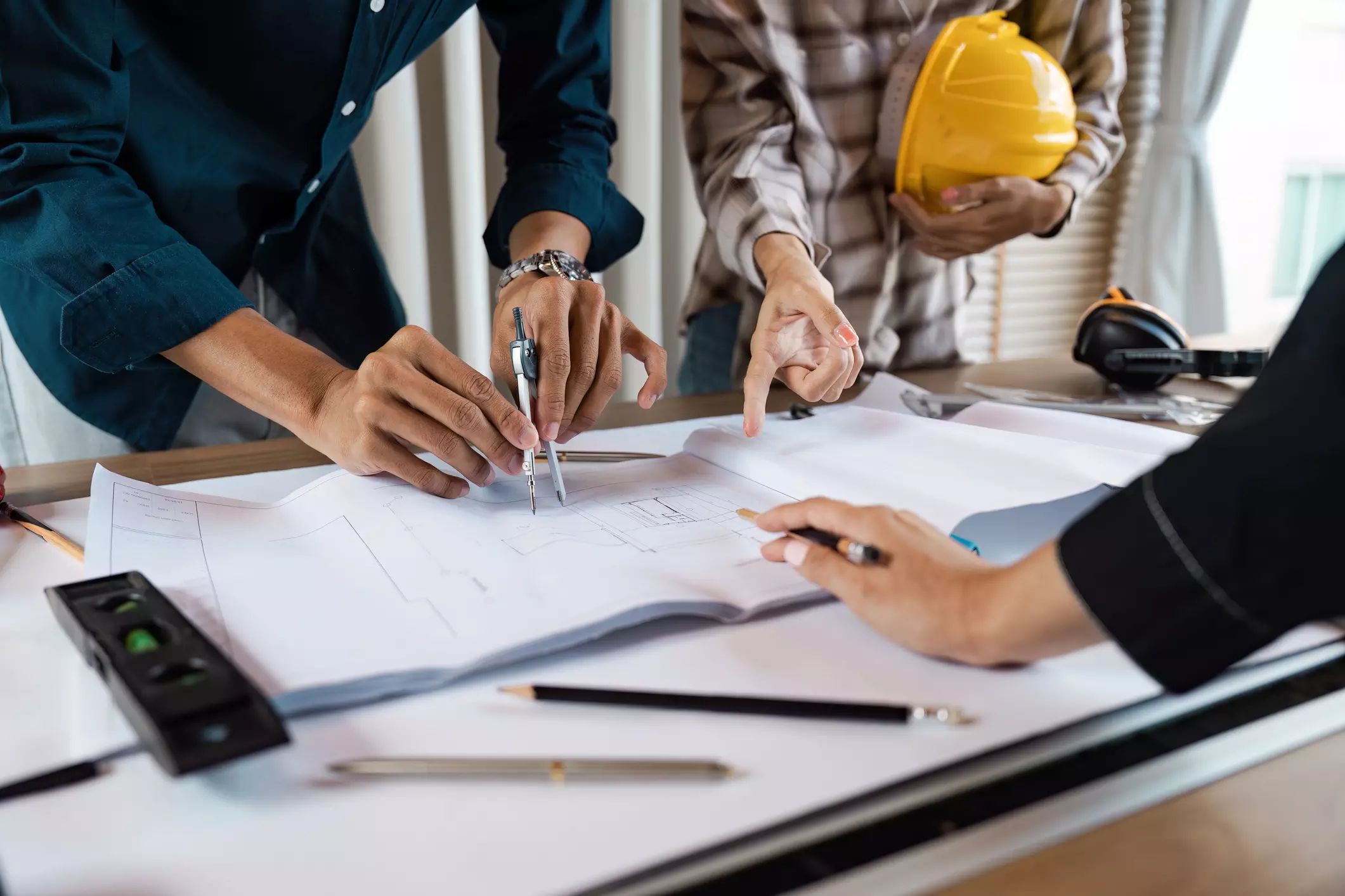 Construction team discussing building plans with compasses and pointing at detailed architectural drawings.